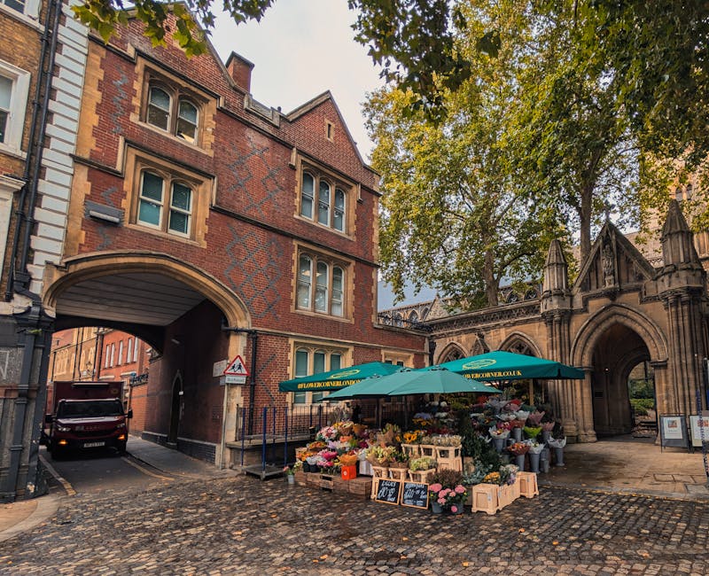 A vibrant flower stall set up beneath large green umbrellas outside a historic brick and stone building near Waterloo Station, London, with a variety of fresh flowers including roses, tulips, and seas