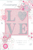 The photograph shows a romantic anniversary card with a soft, intimate atmosphere, reminiscent of a quiet evening walk through Waterloo's side streets. At the centre, the word LOVE is spelled out in large, raised letters that feel plush and tactile to the touch. A fine layer of pale, shimmering glitter dusts each letter, with the 'O' transformed into a subtle, sparkling heart in textured silver, drawing the eye gently inward. The colour palette is built from muted pastel pinks, dusky mauves, and silvery greys, all resting on a smooth blush-pink background that seems to glow faintly, like warm light from a window near the South Bank. Around this focal word, soft, watercolor-style flowers open and curl, their edges blurred just enough to suggest delicacy and movement. The blossoms vary in size, framed by slender stems, curled tendrils, and tiny, swirling flourishes, some shaped like petals in mid-fall and others like faint, fluttering butterflies. Silvery highlights glint along a few petals and leaves, echoing the sheen of fresh foliage in a florist's morning delivery. The composition is airy, with plenty of space around the design, giving a sense of calm and breathing room. In graceful script, the phrases On Our Anniversary and I love you today and always are written in a gentle, flowing hand, as though carefully penned for someone cherished. The overall effect is that of a beautifully arranged paper bouquet, perfect for accompanying floral delivery to a home or riverside apartment in Waterloo, marking an anniversary with understated yet deeply felt warmth.
